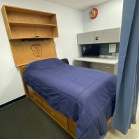Bunk room with a single bed, navy bedding, a wooden headboard with the fire department emblem, and a built-in desk