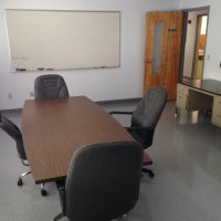 Meeting room with a wooden conference table, black office chairs, and a whiteboard
