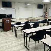 Training classroom with rows of tables and chairs, a podium with the department emblem, and an American flag